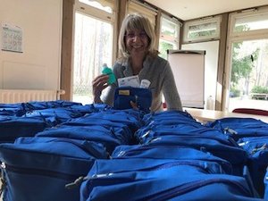 Eine Frau steht lächelnd vor 50 blauen gefüllten Hygienetaschen 